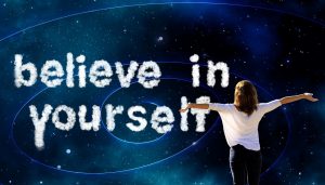 outer space backdrop with a woman facing away holding her arms out with the words believe in yourself